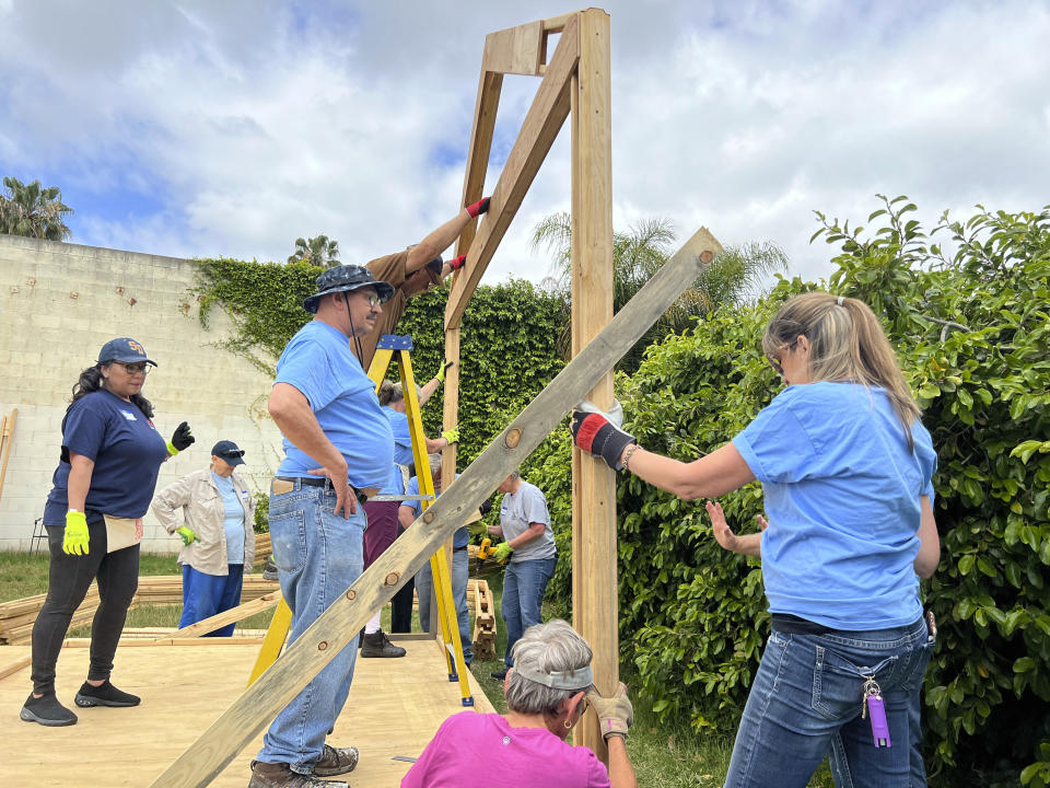 In this photo provided by Amikas, community and church volunteers raise and place the first arch, beginning the framing of cabin four at Meridian Baptist Church in El Cajon, Calif., on April 16, 2022. The Emergency Sleeping Cabins will serve as bridge housing for homeless single mothers with children. (Lisa Kogan/Amikas via AP)