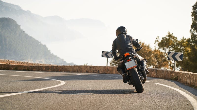 Back shot of man riding sport motorbike taking a curve surrounded by nature at mountain