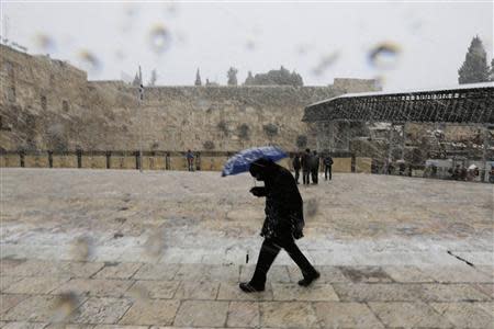 A man holding an umbrella walks as snow falls at the Western Wall in Jerusalem's Old City December 12, 2013. REUTERS/Ammar Awad
