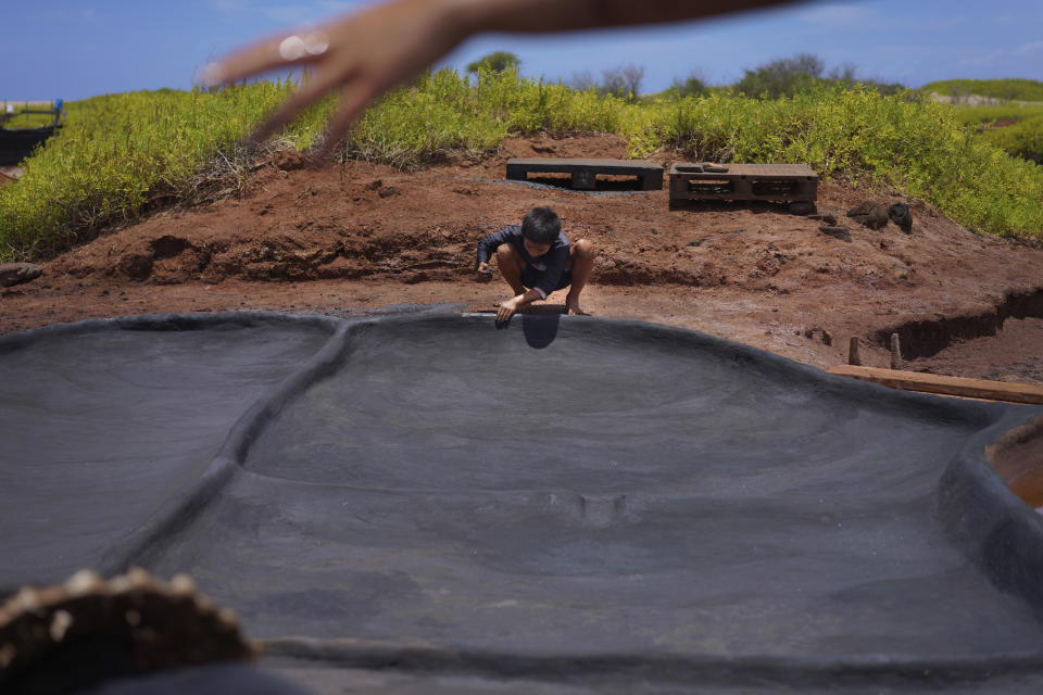 Kekanemekala Taniguchi, son of Tina Taniguchi, smooths wet black clay onto the wall of a salt bed in the Hanapepe salt patch on Wednesday, July 12, 2023, in Hanapepe, Hawaii. 22 Native Hawaiian families work the beds each summer to make "paakai," or Hawaiian salt, which can only be given away or traded, not sold. (AP Photo/Jessie Wardarski)