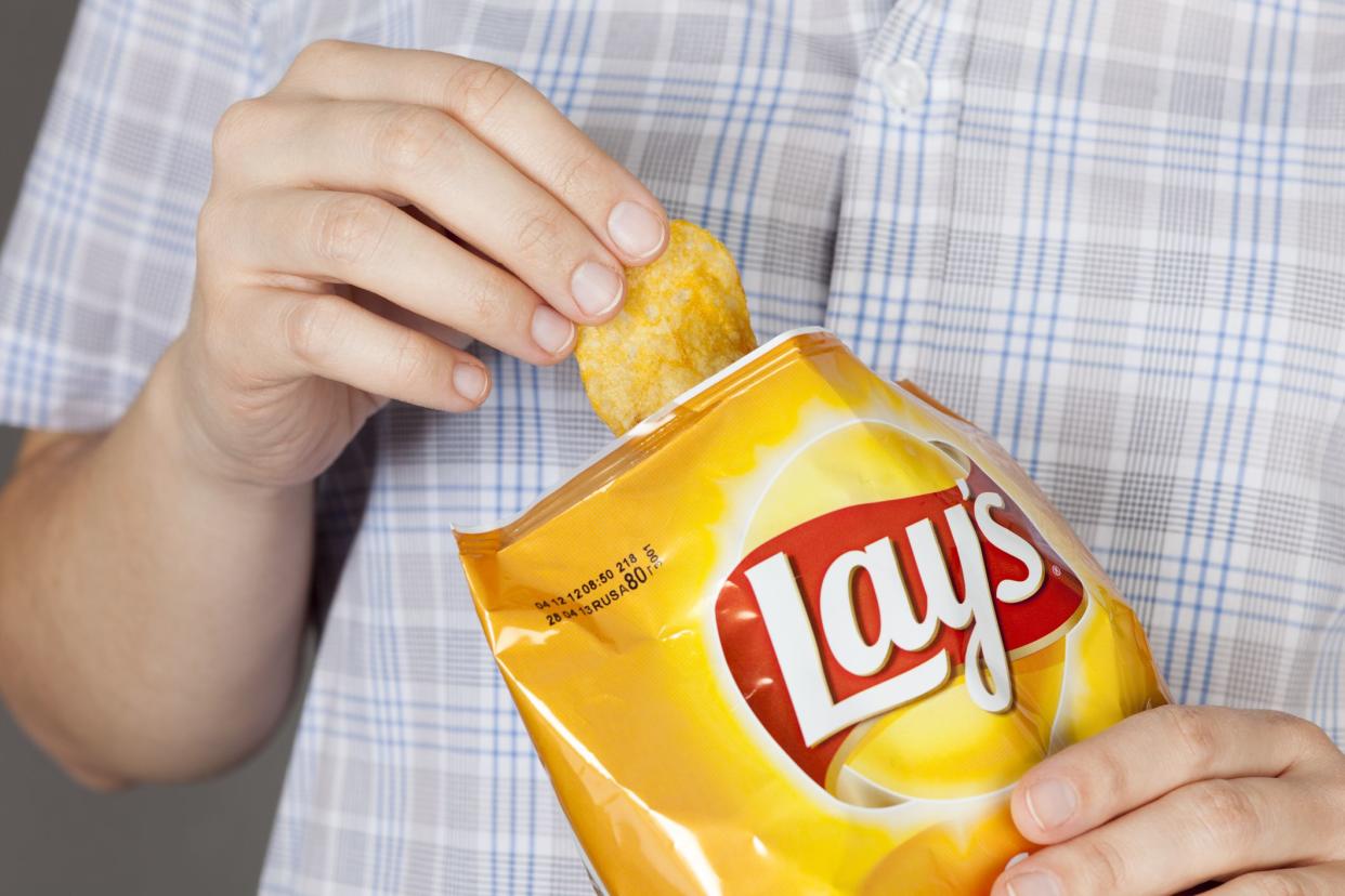 Hand takes out potato chip from Lay's bag