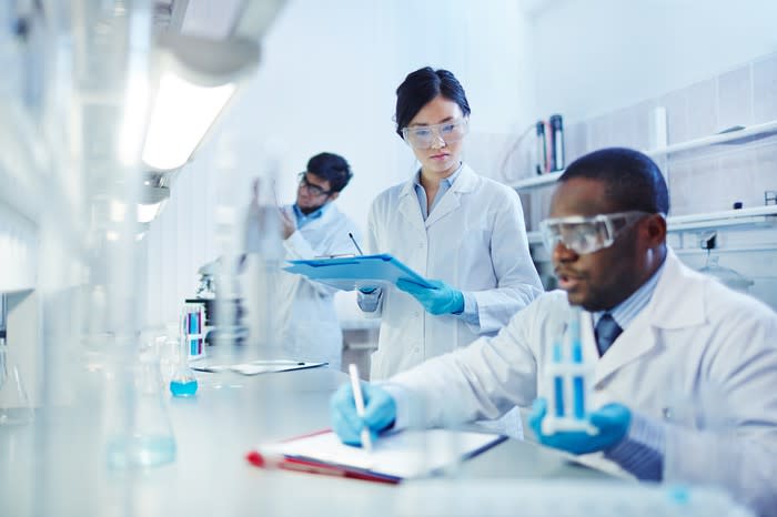 Three people in white lab coats with safety glasses in a lab