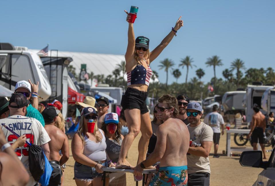 A woman raises her hands in the air as she stands atop a board held by six other people in the stagecoach RV campground
