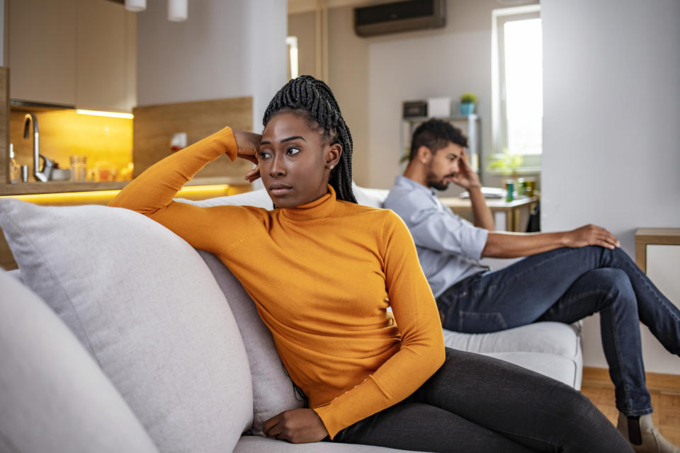 Two people sitting back to back, one on a couch and the other on a chair, both appear upset and not talking