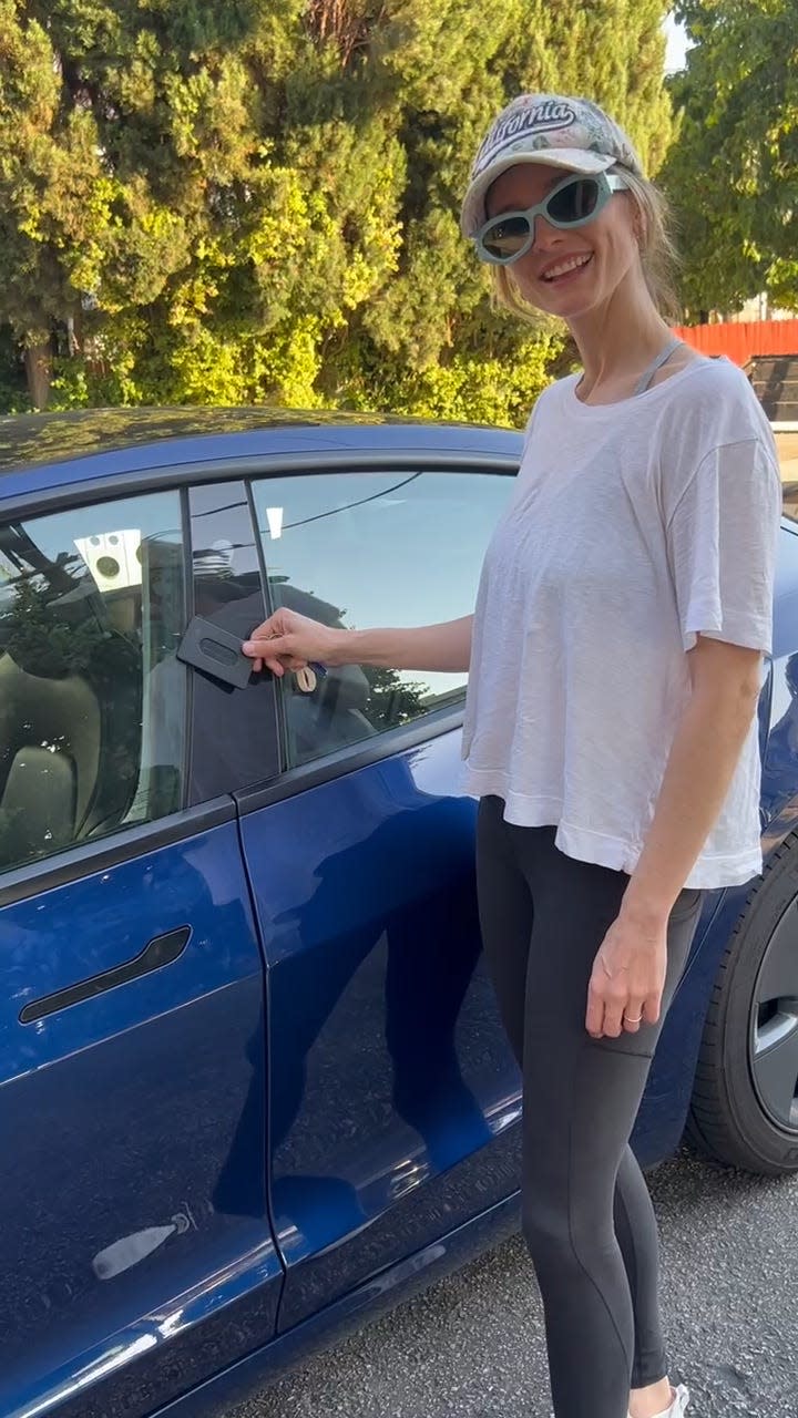 Woman in hat and sunglasses locks her Tesla with a key card.