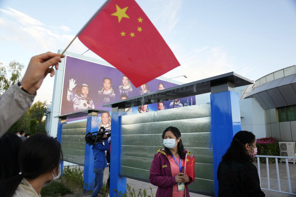 A woman holds up a Chinese flag near a board displaying China's astronauts at the Jiuquan Satellite Launch Center in Jiuquan in northwestern China, Thursday, June 17, 2021. China has launched the first three-man crew to its new space station in its ambitious programs first crewed mission in five years. (AP Photo/Ng Han Guan)