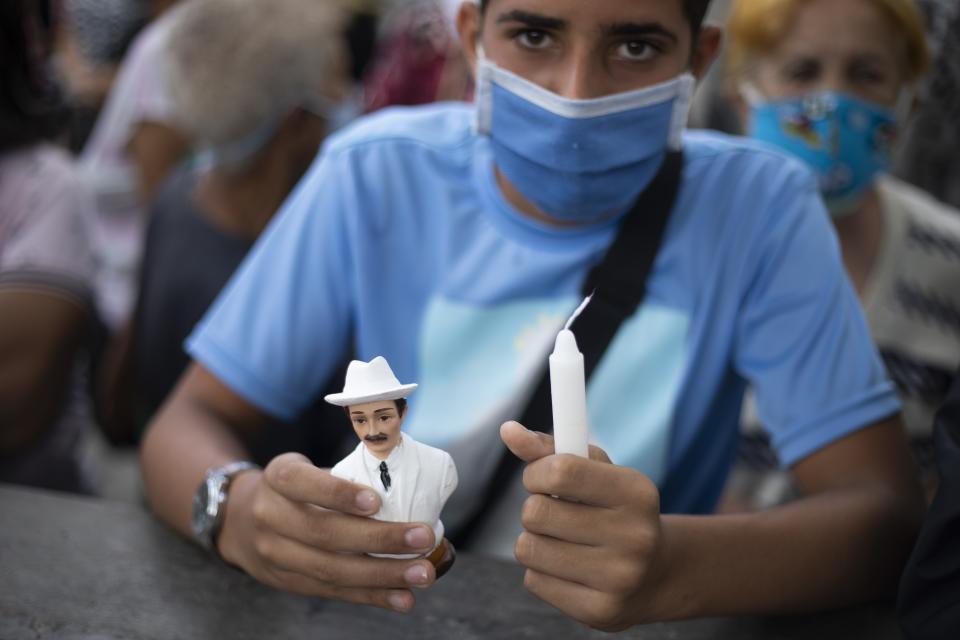 Un devoto del difunto Dr. José Gregorio Hernández sostiene su foto y un rosario afuera de la iglesia La Candelaria donde está enterrado en Caracas, Venezuela, el lunes 26 de octubre de 2020. (AP Foto/Ariana Cubillos)