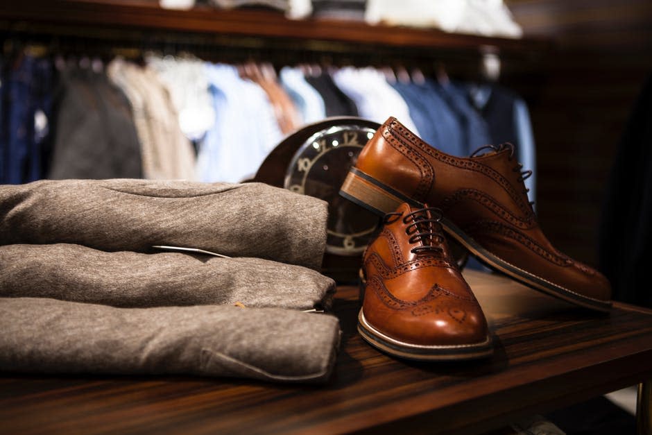 Par De Zapatos De Punta De Ala De Cuero Marrón Junto A Ropa Gris Sobre Superficie De Madera