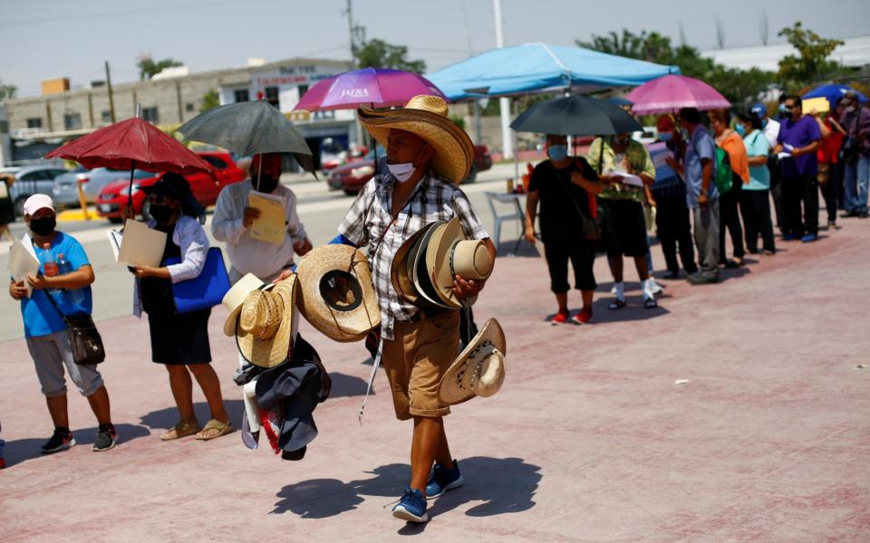 A man sells hats as people queue to receive the Pfizer vaccine, during a mass vaccination program for people over 50 at a baseball stadium in Ciudad Juarez - Reuters