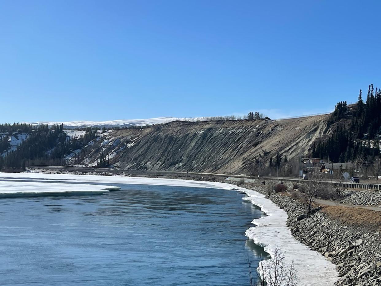 Looking up the Yukon River in Whitehorse, alongside Robert Service Way and the escarpment, in March. The city has been closely monitoring the escarpment this spring after a series of landslides in 2022 and 2023. (Maria Tobin/CBC - image credit)