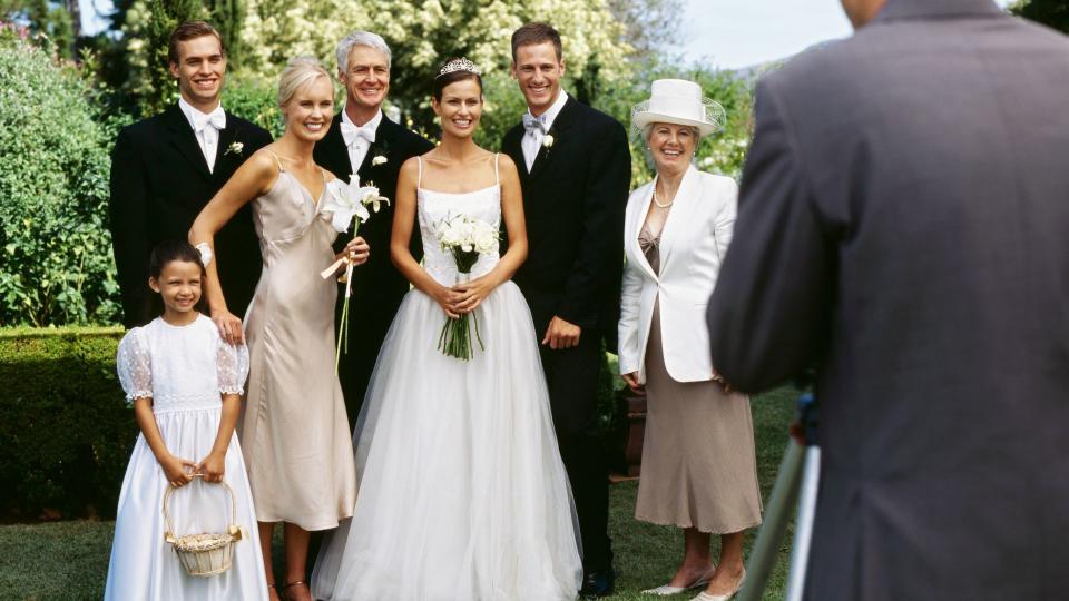 newlywed couple standing with their parents and guests and posing in front of a camera