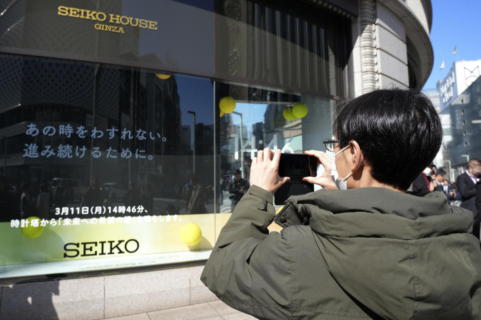 A passerby takes a photo of the sign at a store for an annual tribute for the victims of a 2011 disaster Monday, March 11, 2024, in Tokyo. Japan on Monday marked the 13th anniversary of the massive earthquake, tsunami and nuclear disaster that struck Japan's northeastern coast. The sign in Japanese says, "Not to forget that moment. To move forward." (AP Photo/Eugene Hoshiko)