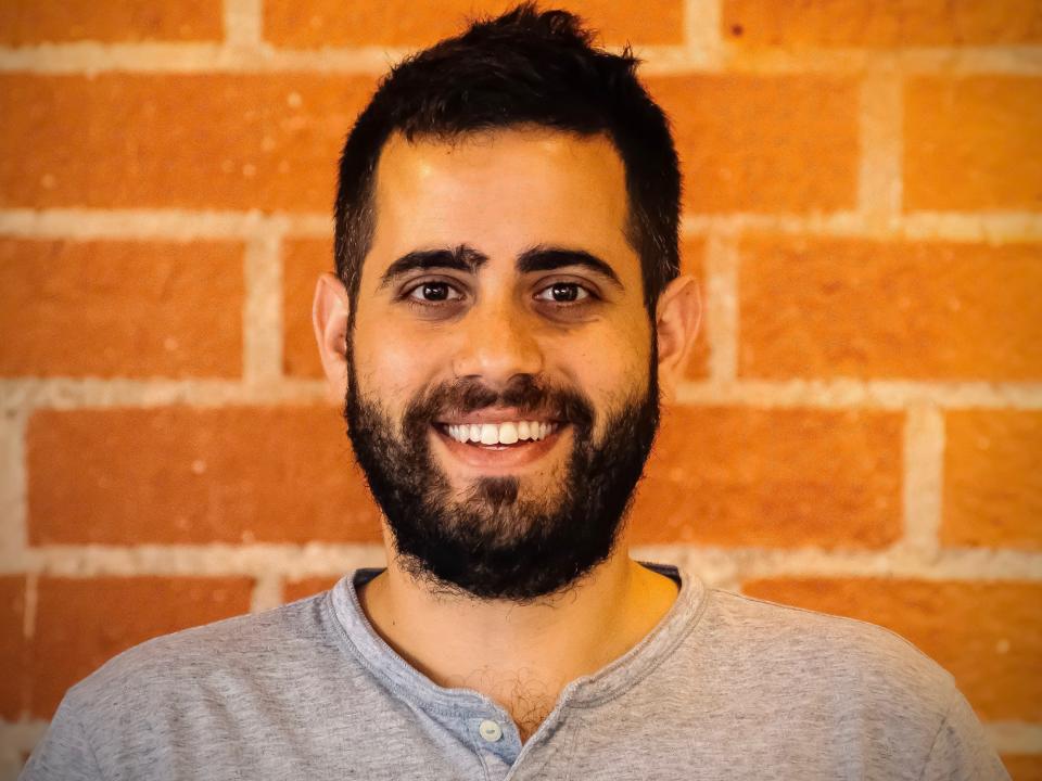 Headshot of Dori Yona smiling and standing against a brick wall