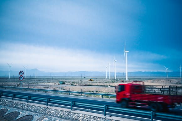 Wind turbines in a field with a red truck on a highway passing in front.