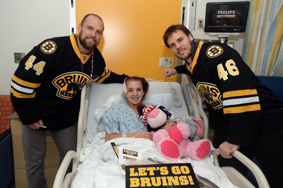 In this Feb. 5, 2015 photo, David Krejci, right, and Dennis Seidenberg of the NHL's Boston Bruins visit with a girl named Carly at Boston Children's Hospital.