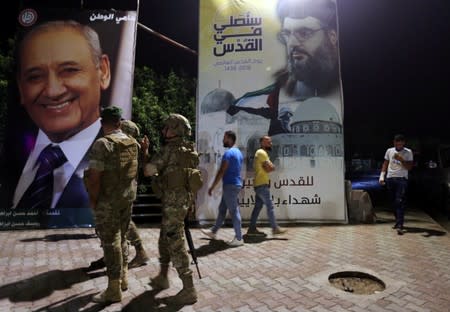 Lebanese army soldiers stand near a poster of Lebanon's Hezbollah leader Sayyed Hassan Nasrallah in Adaisseh village near the Lebanese-Israeli border