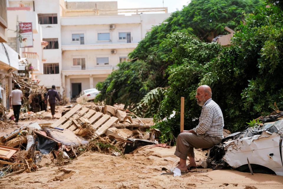 A man sits on a damaged car, after a powerful storm and heavy rainfall hit Libya, in Derna (Esam Omran Al-Fetori  / Reuters)