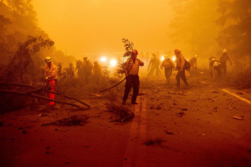 Firefighters battling the Dixie Fire clear Highway 89 after a burned tree fell across the roadway in Plumas County, Calif., on Friday, Aug. 6, 2021.