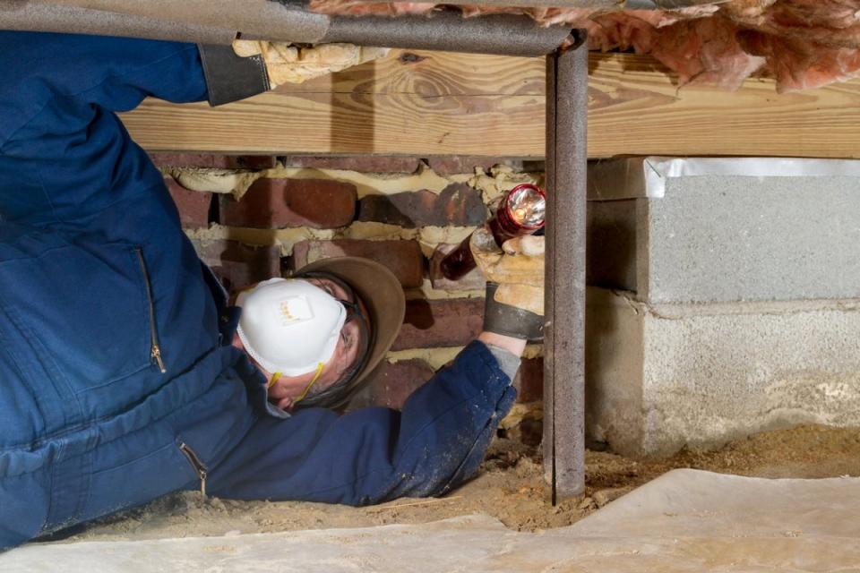 Plumber wearing a mask, putting insulation on a pipe in a crawl space.