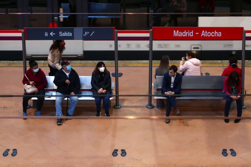 Commuters wearing protective face masks wait on a platform at Atocha train station in Madrid