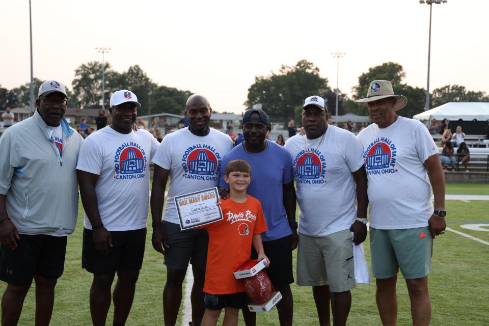 Gareth Gier from Katy, Texas joins a group of Pro Football Hall of Famers to show off prizes he received for traveling the furthest to take part in the Play Football Skills Camp at the Hall of Fame Village's ForeverLawn Sports Complex, Tuesday, Aug. 1, 2023, in Canton.