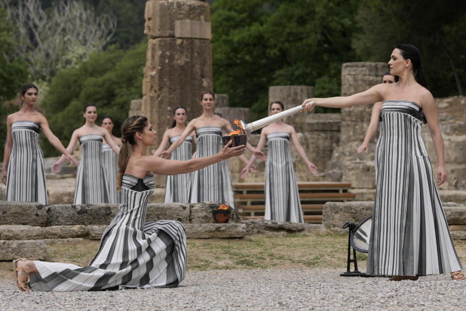 Actress Mary Mina, playing high priestess, right, lights a torch during the official ceremony of the flame lighting for the Paris Olympics, at the Ancient Olympia site, Greece, Tuesday, April 16, 2024. The flame will be carried through Greece for 11 days before being handed over to Paris organizers on April 26. (AP Photo/Thanassis Stavrakis)