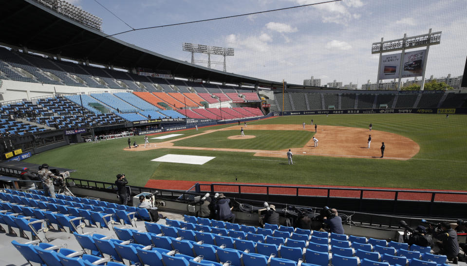 Photographers and TV camera work near empty seats during the pre-season baseball game between Doosan Bears and LG Twins in Seoul, South Korea, Tuesday, April 21, 2020. South Korea's professional baseball league has decided to begin its new season on May 5, initially without fans, following a postponement over the coronavirus. (AP Photo/Lee Jin-man)