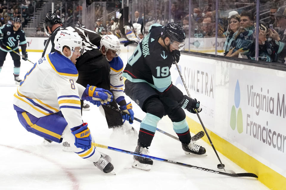 An official tries to get out of the way as Seattle Kraken's Calle Jarnkrok (19) and Buffalo Sabres' Robert Hagg (8) and Cody Eakin try to get control of the puck during the first period of an NHL hockey game Thursday, Nov. 4, 2021, in Seattle. (AP Photo/Elaine Thompson)