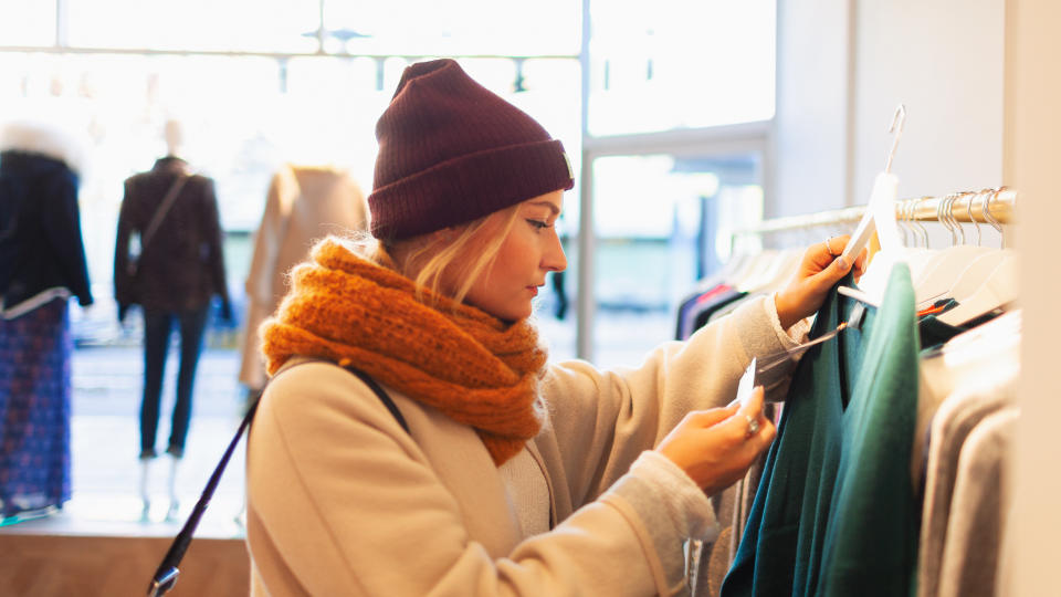 Young woman shopping in clothing store, checking price tag.