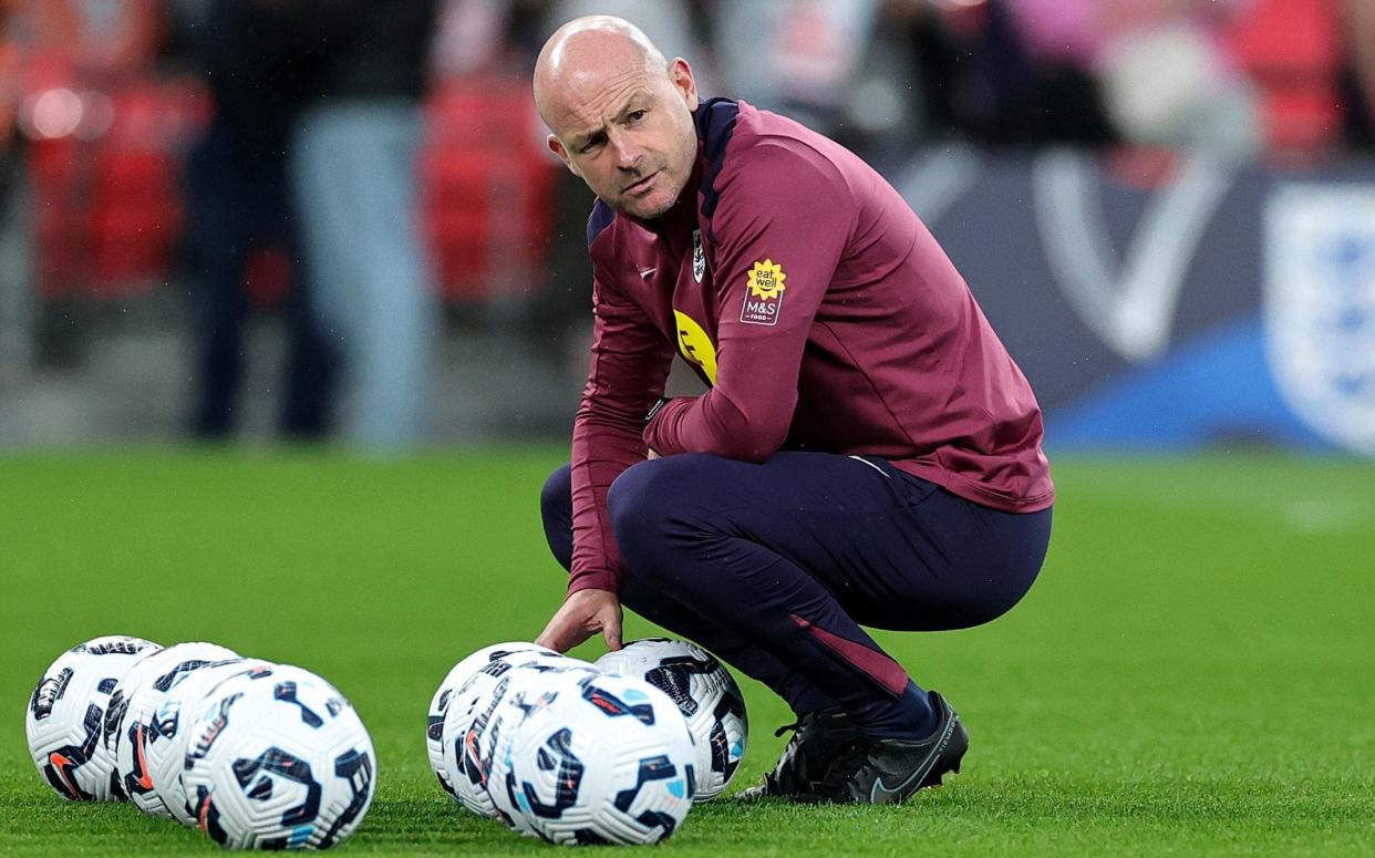 Lee Carsley, the interim manager of England, crouches with footballs and looks on during the warm-up