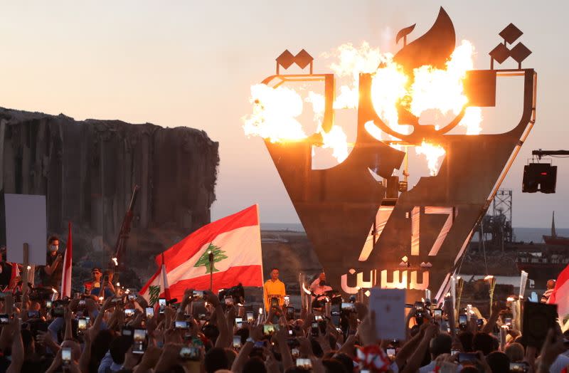 Anti-government demonstrators take pictures of a metal sculpture spelling out the word "revolution" topped by flames during a protest as Lebanese mark one year since the start of nation-wide protests, near Beirut's port