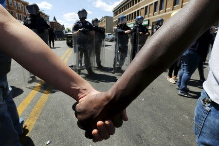 Members of the community hold hands in front of police officers in riot gear outside a recently looted and burned CVS store in Baltimore, Maryland, United States April 28, 2015. REUTERS/Jim Bourg