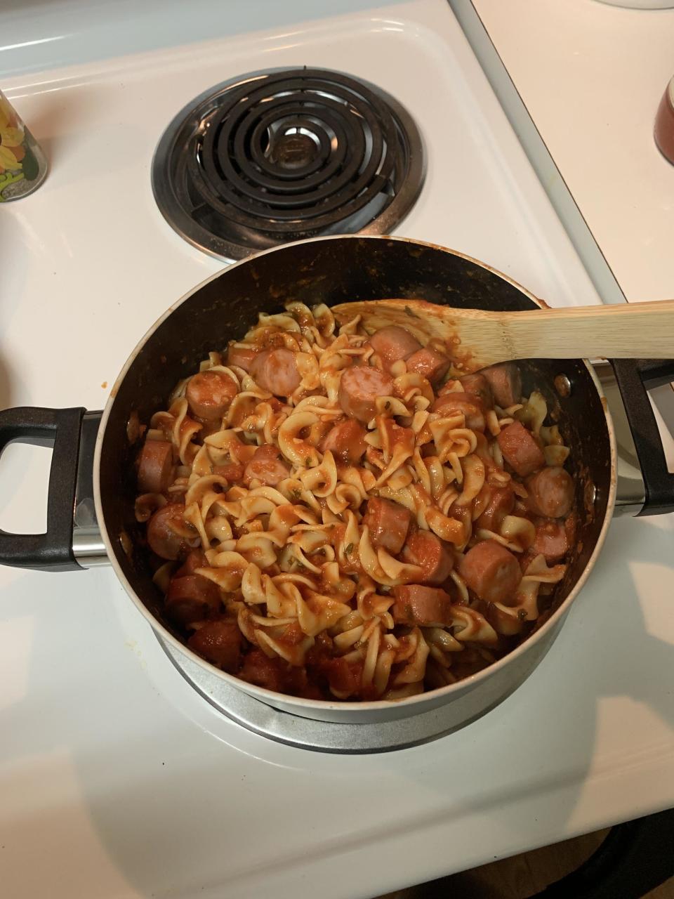 A skillet on a stove containing cooked pasta with sliced sausages and sauce