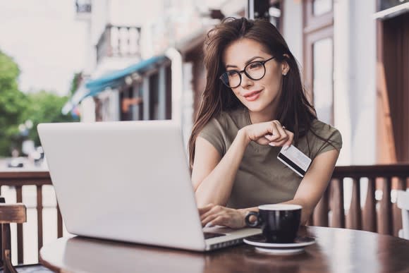 A bespectacled woman shopping online while on her laptop and holding a credit card.