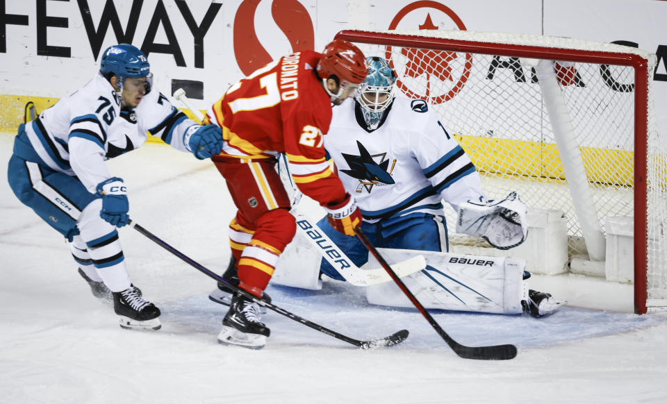 San Jose Sharks goalie Devin Cooley (1) blocks the net on Calgary Flames forward Matthew Coronato (27) as forward Danil Gushchin (75) checks during the second period of an NHL hockey game Thursday, April 18, 2024, in Calgary, Alberta. (Jeff McIntosh/The Canadian Press via AP)