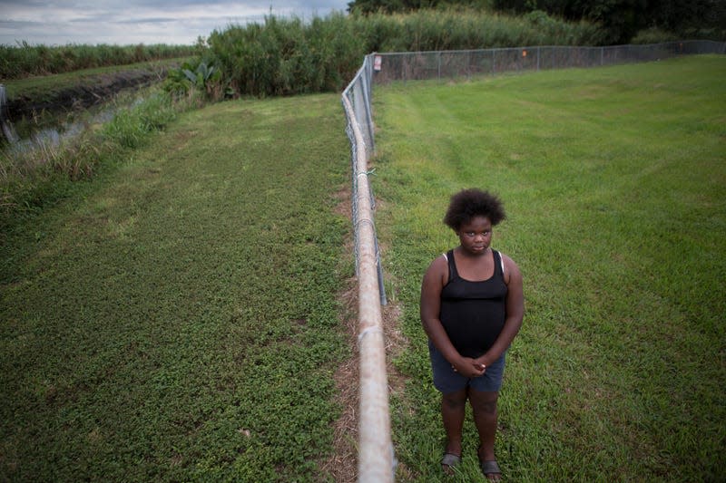 In this Nov. 4, 2019 photo, Kaniyah Patterson stands in front of a sugar cane field behind her home in Pahokee, Fla. Patterson says that smoke from sugar cane burns trigger her asthma. For generations, Florida’s sugar cane farmers have legally set fire to their fields prior to harvest. But the smoke is a nuisance for predominantly poor communities near the fields.