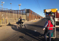 In this Jan. 10, 2020, photo, a snack vendor stands on a street as a cyclist goes by in San Luis Rio Colorado, Mexico, leading to a border crossing in San Luis, Ariz. Months earlier, asylum seekers waited in line in tents in San Luis Rio Colorado, Mexico. Illegal border crossings have plummeted as the Trump administration extended a policy to make asylum seekers wait in Mexico for court hearings in the U.S. (AP Photo/Elliot Spagat)