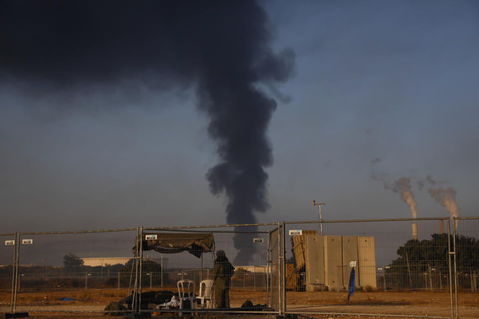 An Israeli soldier stands guard next to an Iron Dome air defense system as smoke rises from an oil tank on fire after it was hit by a rocket fired from Gaza Strip, near the town of Ashkelon, Israel, Wednesday, May 12, 2021. (AP Photo/Ariel Schalit)