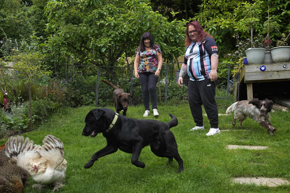 Avril Clark, left, and Lucy watch their dogs playing with chickens at their house in London, Tuesday, June 11, 2024. Avril Clark operates the group Distinction Support, a U.K.-based global online network that helps people whose partner went through or is undergoing a gender transition. Her spouse, a British soccer referee at the time, came out publicly as transgender in 2018, changed her name to Lucy and brought the couple much attention. Avril Clark says that until then, they kept their arrangement private and "lived a double life" for 15 years. (AP Photo/Kin Cheung)