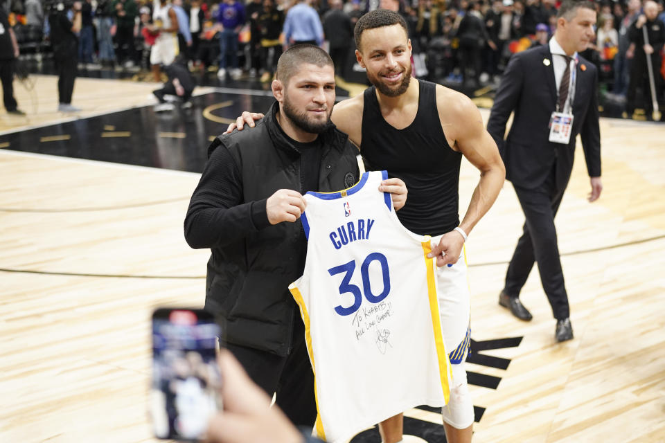 Golden State Warriors guard Stephen Curry (30) presents former Khabib Nurmagomedov, left, a former mixed martial arts fighter, with a signed jersey after the Warriors' NBA basketball game against the Toronto Raptors on Friday, March 1, 2024, in Toronto. (Arlyn McAdorey/The Canadian Press via AP)