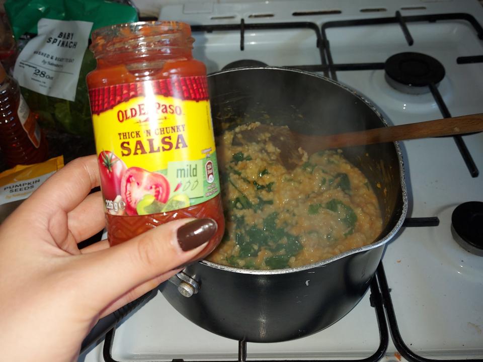 An open jar of salsa ready to be added to a saucepan of savory oats, carrot, and kale.