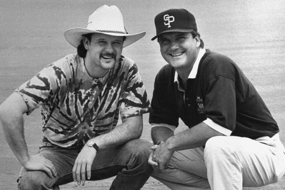 musician Tim McGraw w. father, former baseball player Tug McGraw in baseball cap, as they crouch next to home plate on baseball field.