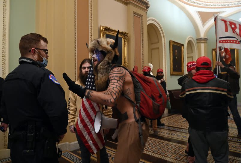 A US Capitol police officer talks to supporters of US President Donald Trump, including Jake Angeli (R), a QAnon supporter known for his painted face and horned hat, that entered the Capitol on January 6, 2021, in Washington, DC. – Demonstrators breeched security and entered the Capitol as Congress debated the a 2020 presidential election Electoral Vote Certification. (Photo by Saul LOEB / AFP) (Photo by SAUL LOEB/AFP via Getty Images)