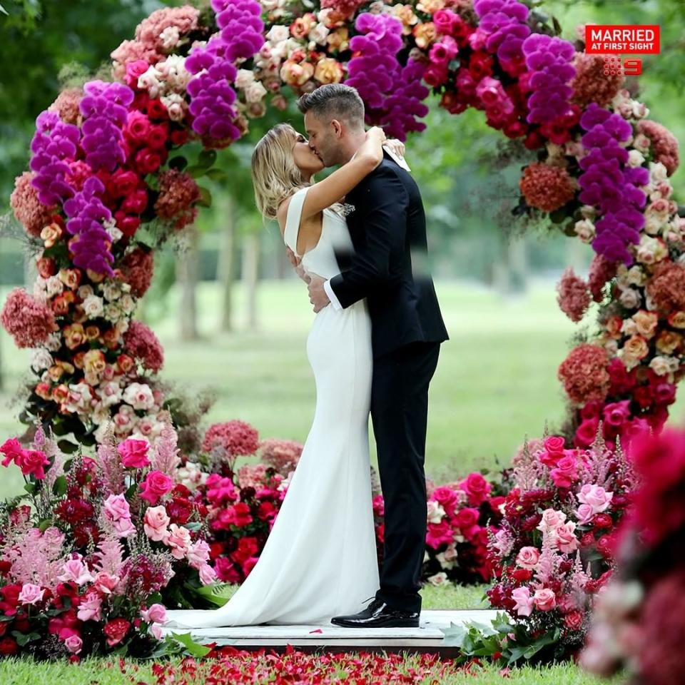 Jake and Bec on their MAFS wedding day under a flower arch