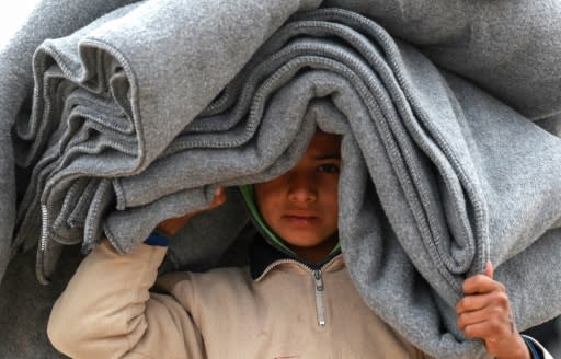 A young boy, who fled the embattled Islamic State group enclave in eastern Syria, carries blankets at a camp for the displaced set up by the US-backed Syrian Democratic Forces