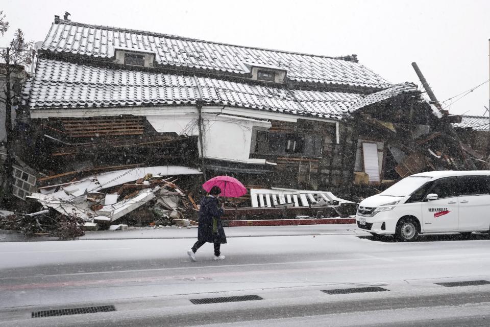 A person walks in the snow through a street near a damaged house in Wajima in the Noto peninsula facing the Sea of Japan, northwest of Tokyo, Sunday, Jan. 7, 2024. Monday's temblor decimated houses, twisted and scarred roads and scattered boats like toys in the waters, and prompted tsunami warnings. (AP Photo/Hiro Komae)