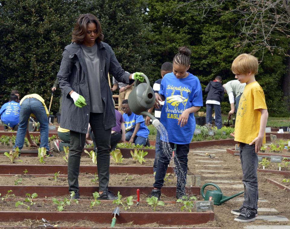 First lady Michelle Obama holds a watering can after she and Friendship Public Charter Elementary School student Dynasty Meade, center, and Bancroft Elementary School student Silas Stutz, right, planted broccoli in the White House Kitchen Garden at the White House in Washington, Wednesday, April 2, 2014. (AP Photo/Susan Walsh)