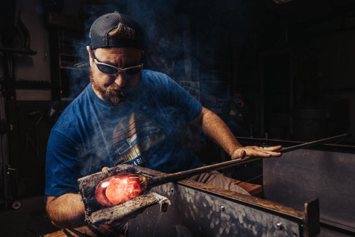 Erich Minton uses damp newspaper to shape glass in his glassblowing shop in Bartlesville. Erich has been working with glass for over 18 years and was first introduced to glassblowing at Central College in Pella, Iowa, where he graduated as an art major.