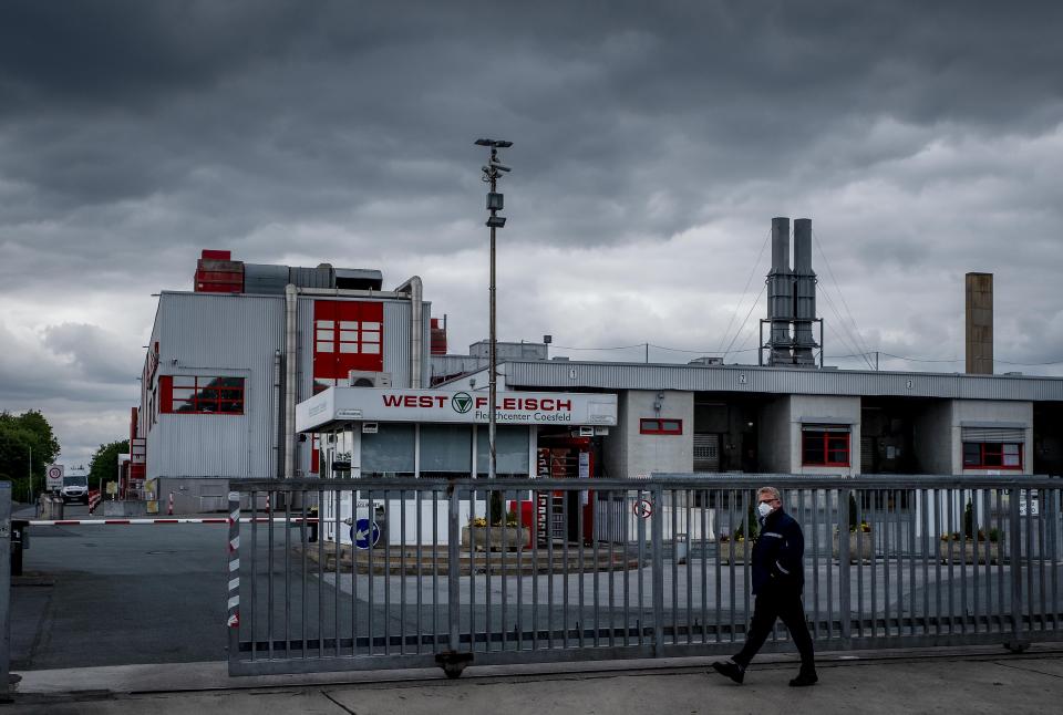 FILE - In this Tuesday, May 12, 2020 file photo a man walks past the Westfleisch slaughterhouse in Coesfeld, Germany. The German government agreed Wednesday to ban the use of subcontractors and increase fines for breaches of labor law in the meat industry starting next year following a series of coronavirus outbreaks linked to abattoirs in recent weeks. (AP Photo/Michael Probst, file)