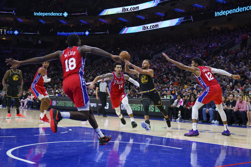 Golden State Warriors' Stephen Curry, center right, passes the ball while surrounded by Philadelphia 76ers during the first half of an NBA basketball game, Saturday, Dec. 11, 2021, in Philadelphia. (AP Photo/Chris Szagola)